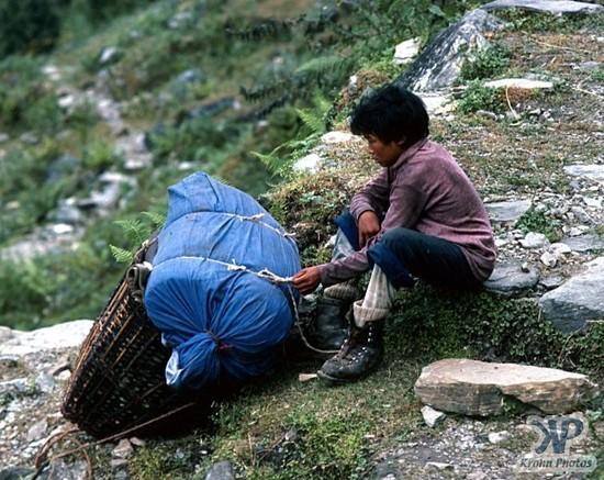 brown child carries huge pack for wealthy mountaineer